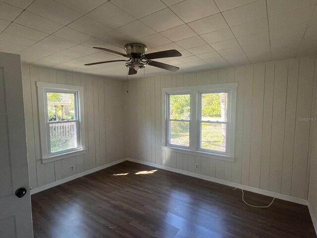 empty room featuring a healthy amount of sunlight, dark wood-style floors, ceiling fan, and baseboards