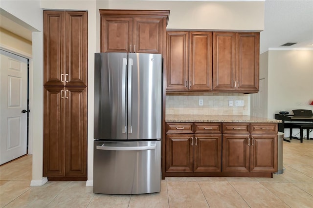 kitchen featuring light tile patterned floors, light stone counters, tasteful backsplash, and freestanding refrigerator