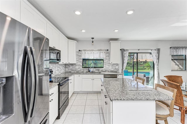 kitchen featuring a kitchen bar, a center island, white cabinets, black appliances, and light stone countertops