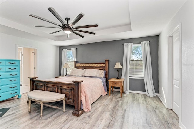 bedroom featuring light hardwood / wood-style floors, ceiling fan, multiple windows, and a raised ceiling