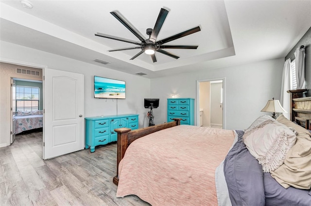 bedroom featuring light hardwood / wood-style floors, ceiling fan, ensuite bathroom, and a tray ceiling