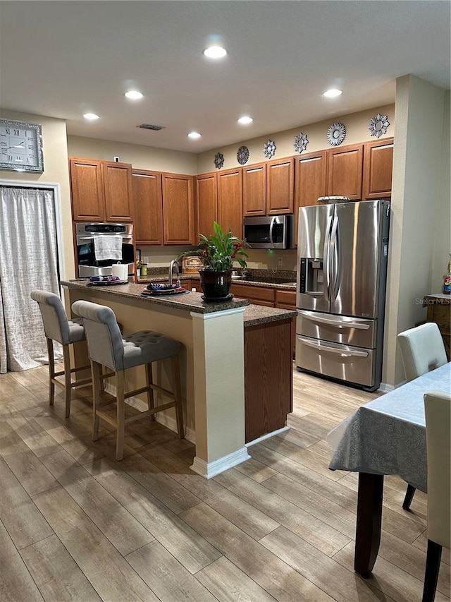 kitchen featuring stainless steel appliances, sink, a breakfast bar area, a kitchen island with sink, and light hardwood / wood-style flooring