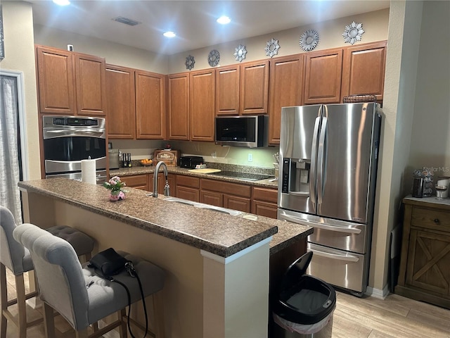 2271 50th Street Cir E, Palmetto, FL 34221 - kitchen with stainless steel appliances, a kitchen breakfast bar, brown cabinetry, light wood-style floors, and recessed lighting