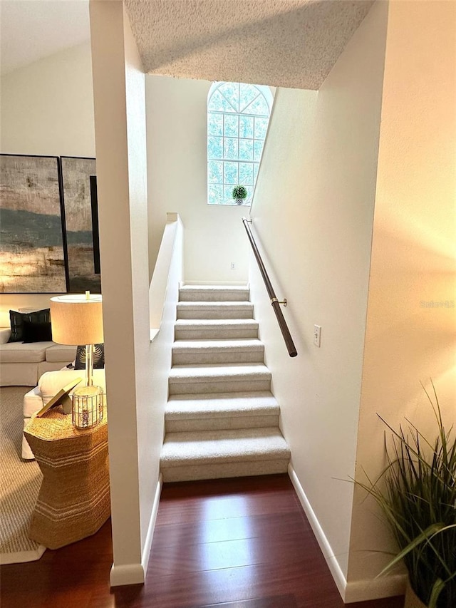 stairs with a textured ceiling, baseboards, and wood finished floors