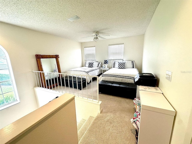 carpeted bedroom with a textured ceiling, multiple windows, and visible vents