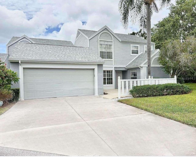 view of front of property featuring roof with shingles, concrete driveway, a front yard, fence, and a garage