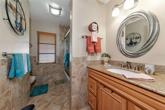 full bathroom featuring combined bath / shower with glass door, toilet, tile walls, and vanity