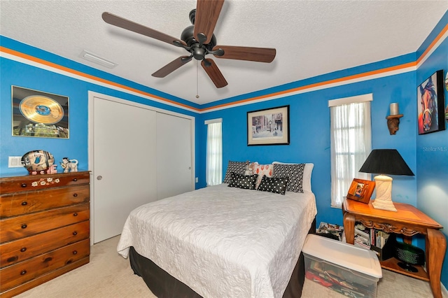 bedroom featuring a textured ceiling, light colored carpet, a closet, and ceiling fan