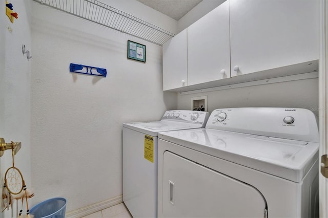 clothes washing area with a textured ceiling, washer and clothes dryer, cabinets, and light tile patterned flooring