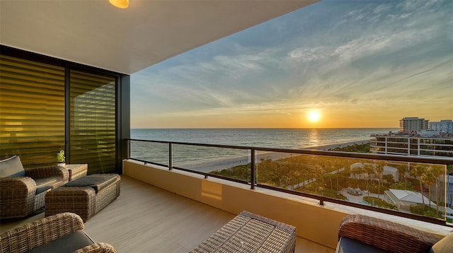 balcony at dusk featuring a view of the beach and a water view