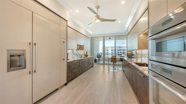 kitchen featuring light hardwood / wood-style floors, dark brown cabinetry, tasteful backsplash, floor to ceiling windows, and ceiling fan