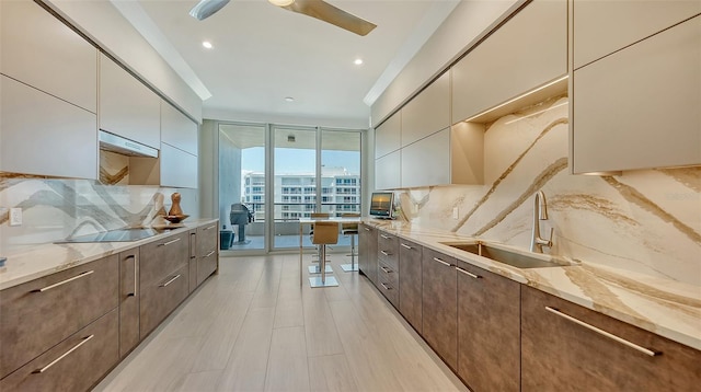 kitchen featuring black electric stovetop, light stone counters, decorative backsplash, sink, and a wall of windows