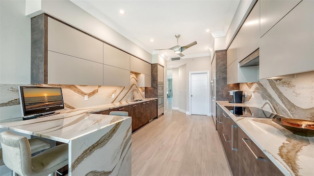 kitchen featuring light hardwood / wood-style floors, black electric stovetop, light stone counters, sink, and ceiling fan