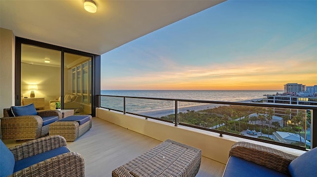 balcony at dusk with outdoor lounge area, a water view, and a beach view