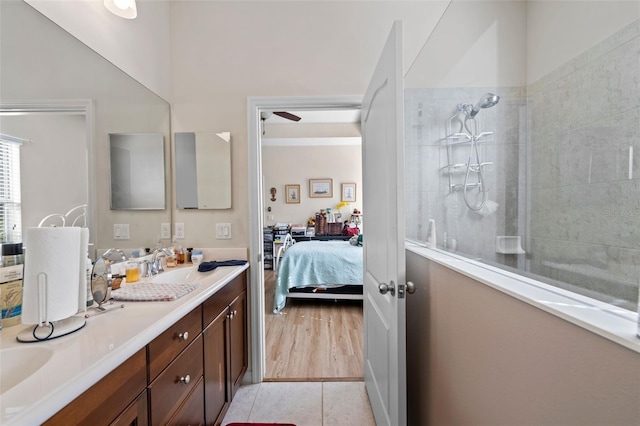 bathroom with a tile shower, vanity, ceiling fan, and wood-type flooring