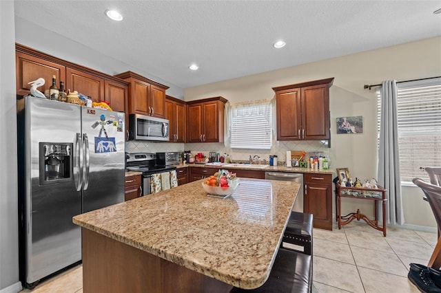 kitchen featuring plenty of natural light, a kitchen island, light stone countertops, and stainless steel appliances