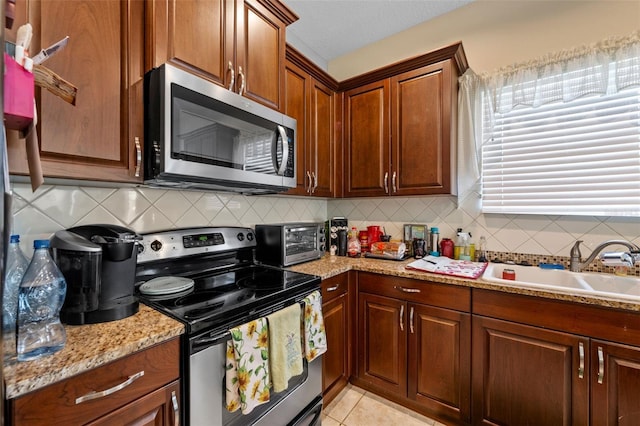 kitchen with sink, light stone counters, decorative backsplash, light tile patterned flooring, and appliances with stainless steel finishes