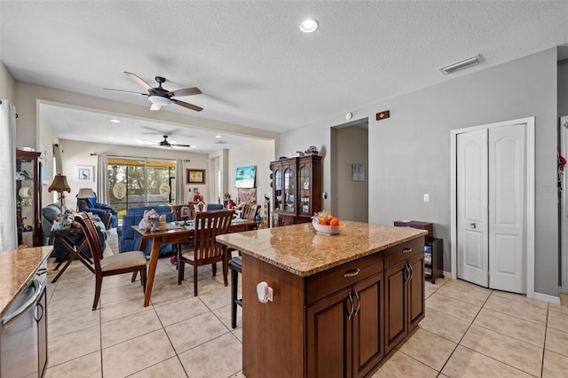 kitchen with ceiling fan, a kitchen island, light tile patterned floors, and a textured ceiling