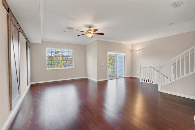 unfurnished living room with a barn door, dark hardwood / wood-style floors, ceiling fan, and ornamental molding