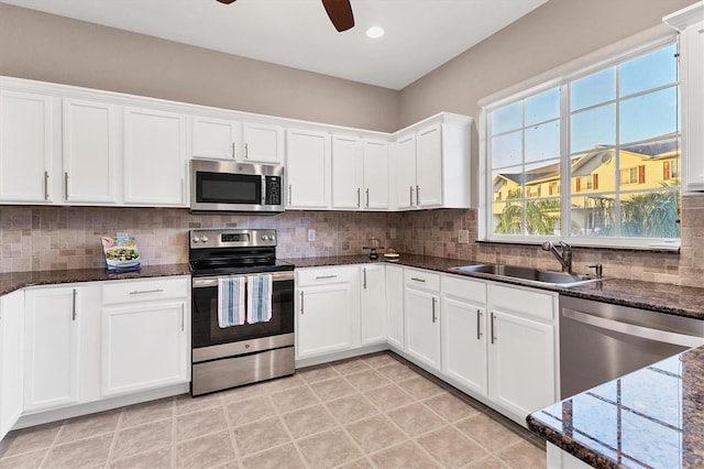 kitchen featuring decorative backsplash, dark stone counters, stainless steel appliances, sink, and white cabinetry