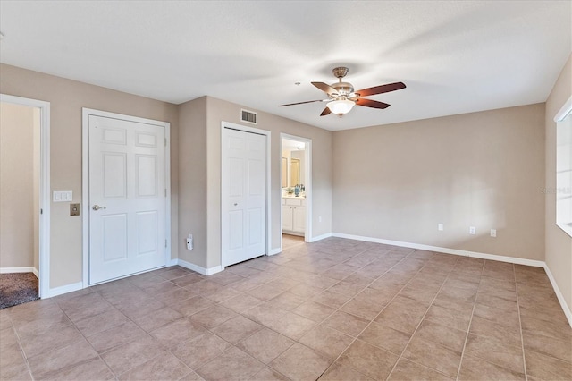 unfurnished bedroom with light tile patterned floors, ensuite bath, and ceiling fan