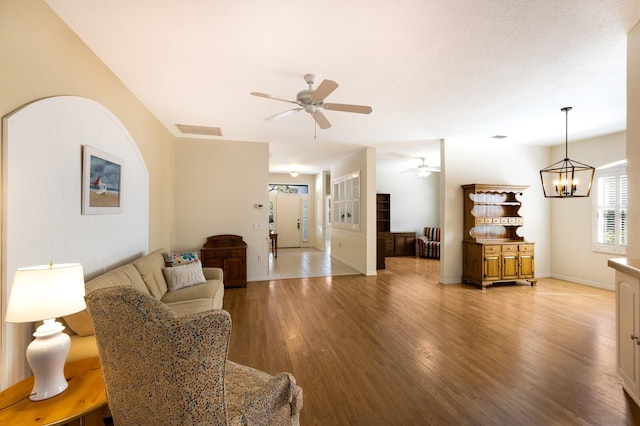 living room with light wood-type flooring and ceiling fan with notable chandelier