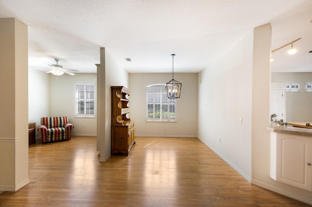 unfurnished room featuring ceiling fan with notable chandelier, a textured ceiling, and light hardwood / wood-style flooring