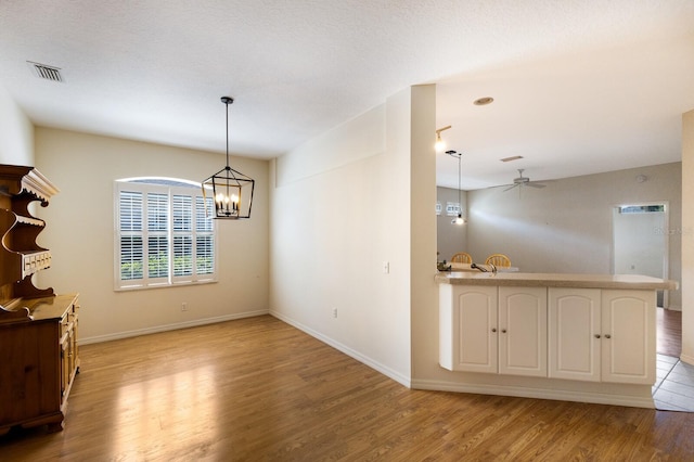 unfurnished dining area featuring ceiling fan with notable chandelier, light hardwood / wood-style flooring, and a textured ceiling