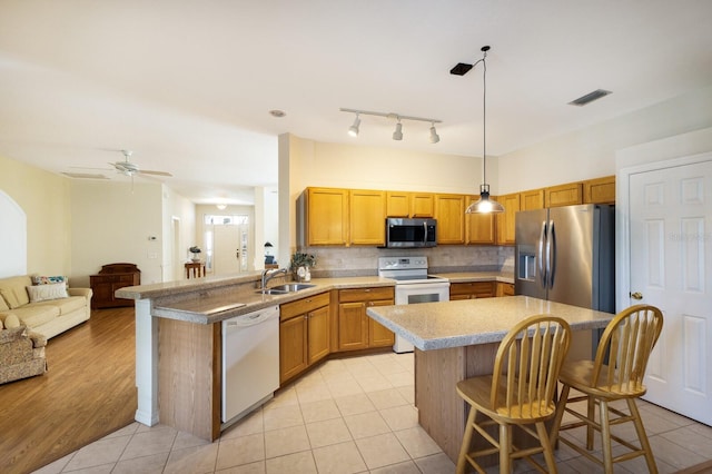 kitchen with sink, a breakfast bar, appliances with stainless steel finishes, hanging light fixtures, and light wood-type flooring