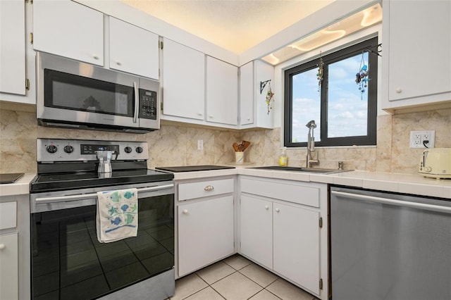 kitchen featuring sink, white cabinetry, light tile patterned floors, stainless steel appliances, and backsplash