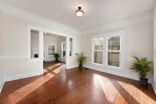 spare room with ornamental molding, ornate columns, and dark wood-type flooring