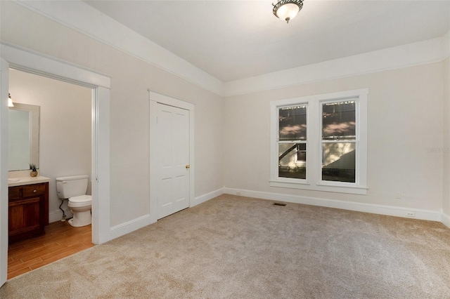 unfurnished bedroom featuring light carpet and ensuite bathroom