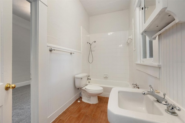 bathroom featuring washtub / shower combination, baseboards, toilet, a sink, and wood finished floors