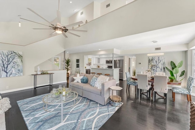 living room with ceiling fan, a towering ceiling, and dark wood-type flooring