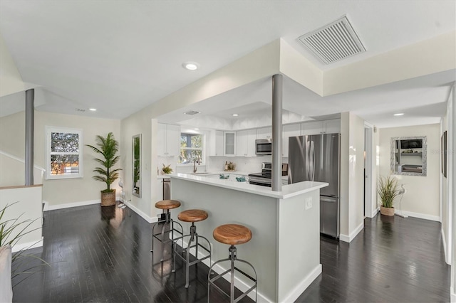 kitchen with a kitchen breakfast bar, sink, dark hardwood / wood-style floors, white cabinetry, and stainless steel appliances