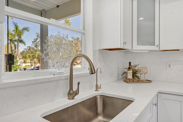 interior details featuring decorative backsplash, sink, white cabinets, and light stone counters