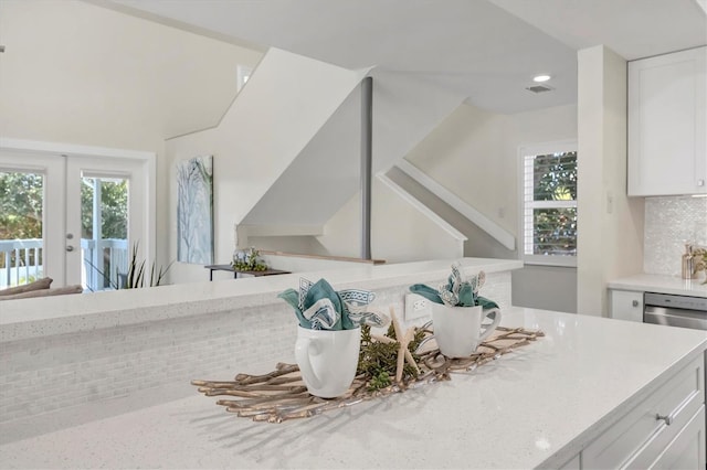 interior details with dishwasher, french doors, light stone counters, decorative backsplash, and white cabinets