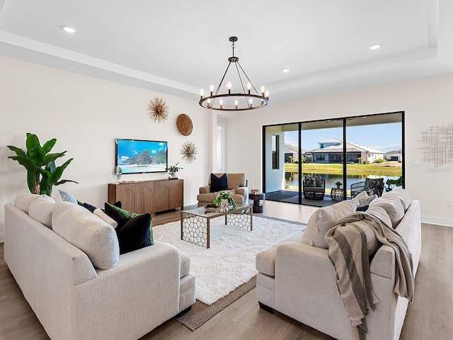 living room featuring light wood-type flooring, a tray ceiling, and a notable chandelier