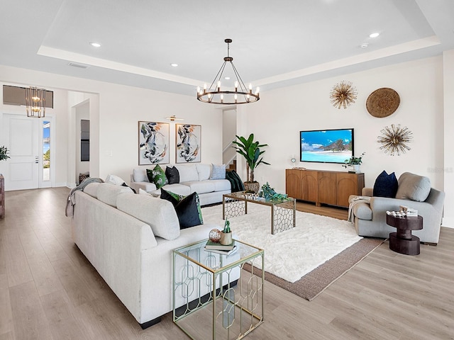 living room featuring a tray ceiling, light hardwood / wood-style floors, and a notable chandelier