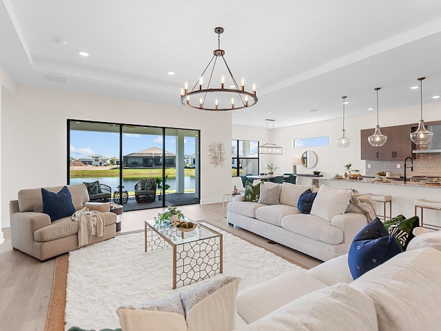 living room featuring a water view, an inviting chandelier, light hardwood / wood-style floors, and sink