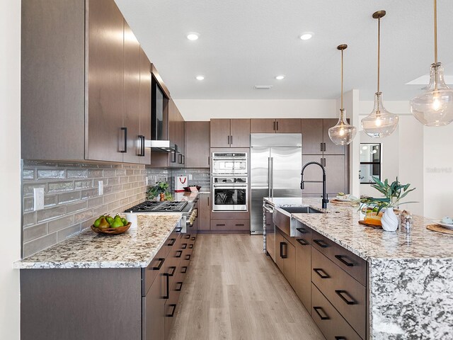 kitchen featuring sink, light hardwood / wood-style flooring, appliances with stainless steel finishes, decorative light fixtures, and dark brown cabinets