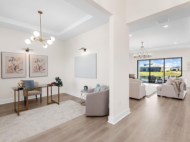 living room featuring a raised ceiling, light hardwood / wood-style flooring, and an inviting chandelier