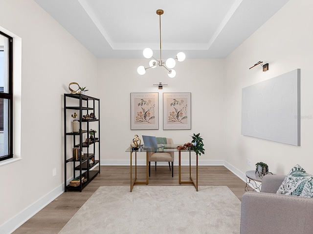 office space featuring a tray ceiling, a healthy amount of sunlight, a notable chandelier, and hardwood / wood-style flooring