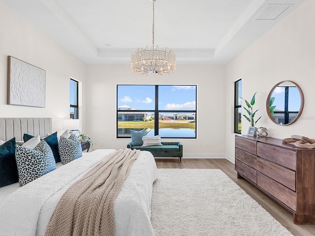 bedroom featuring a raised ceiling, hardwood / wood-style floors, and an inviting chandelier