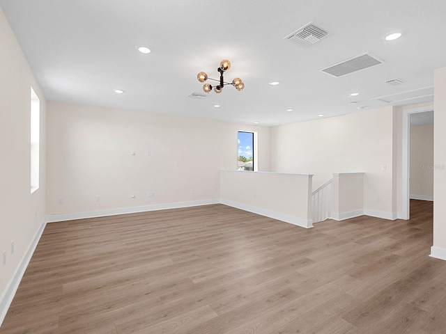 empty room with light hardwood / wood-style floors and an inviting chandelier