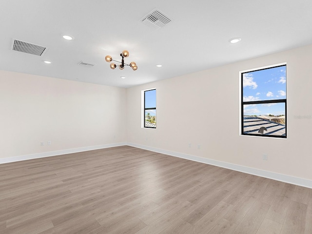 unfurnished room featuring a notable chandelier and light wood-type flooring