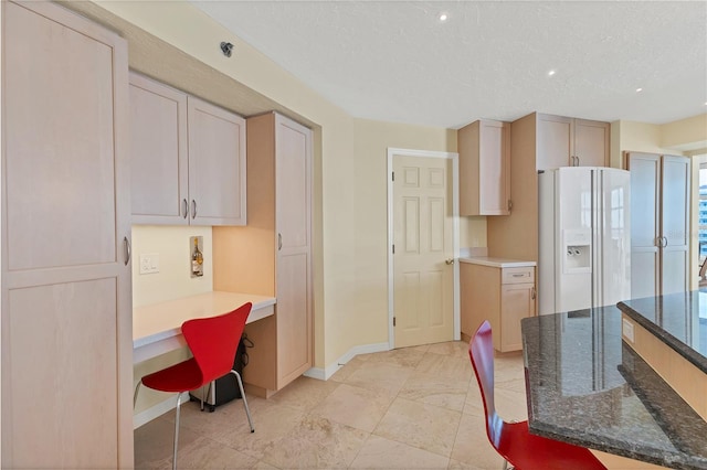 kitchen with light brown cabinets, dark stone counters, built in desk, white fridge with ice dispenser, and a textured ceiling