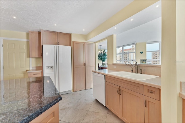 kitchen featuring sink, dark stone counters, a textured ceiling, white appliances, and light brown cabinetry