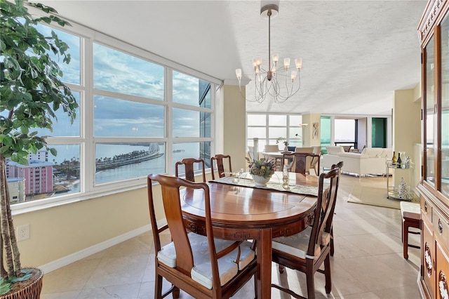 tiled dining area featuring a notable chandelier, a water view, and a textured ceiling