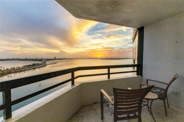 balcony at dusk featuring a water view